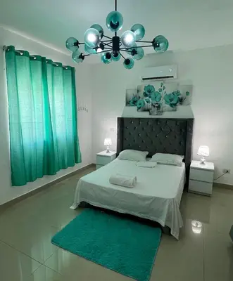 a bedroom with a bed with green curtains and a chandelier at Paisible et confo in Boca Chica