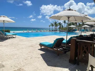 a swimming pool with chairs and an umbrella and the ocean at Beach Golf penthouse Arena Gorda Beach P C in Punta Cana