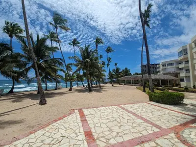 a sandy beach with palm trees and a building at Apartamento frente al mar en Albatros in Villas del Mar