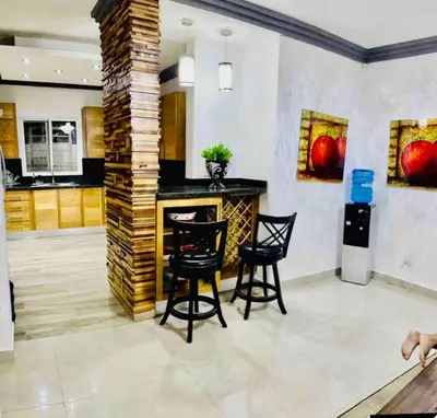 a kitchen with a bar with chairs and paintings on the wall at Hermosa Casa familiar en las orquideas LR in La Romana