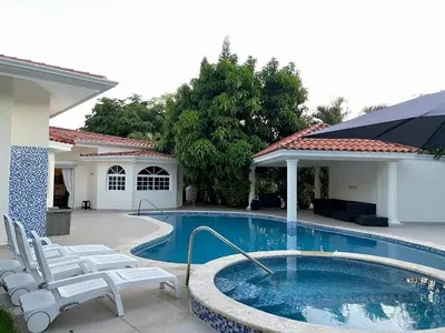 a swimming pool with white chairs next to a house at Villa in Metro Country Club, Juan Dolio in Juan Dolio
