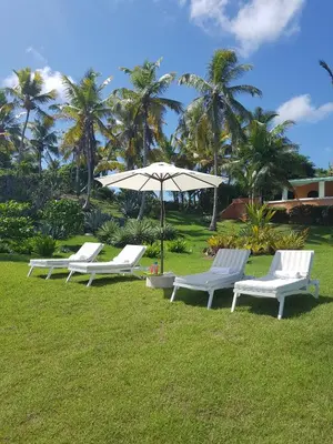 three white lounge chairs and an umbrella in a field at Villa Los Gorgones in Las Galeras