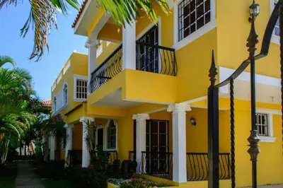 a yellow building with balconies and palm trees at The Three Sisters Villa in Puerto Plata