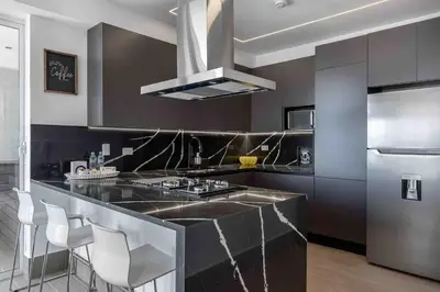 a kitchen with a black counter and a stainless steel refrigerator at ®{LUX~City~Skyline} @DowntownSD PrivéJaccuziGym in Santo Domingo