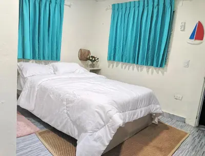 a bedroom with a white bed with blue curtains at Habitacion cerca de la Playa in Boca Chica