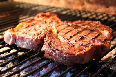 two pieces of steak cooking on a grill at Aparta Hotel Azzurra in Boca Chica