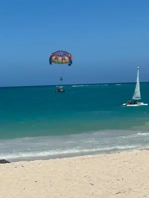 a parachute is flying over the ocean with a sail boat at Apartment Punta Cana Oasis ONA Residences in Punta Cana