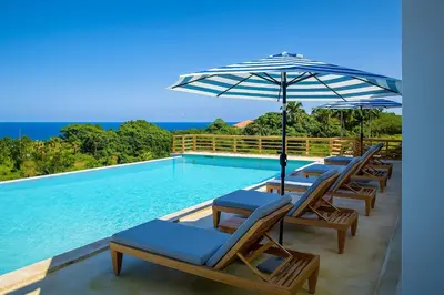 a row of chairs and an umbrella next to a swimming pool at Private Villa-Infinity Pool-26 guests capacity-14 King Size Beds-8 bedrooms-8 and half baths in Cabrera
