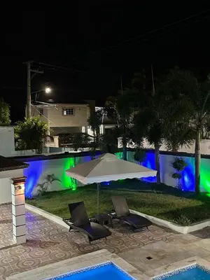 an umbrella and chairs next to a swimming pool at night at villa fortuna in Nagua