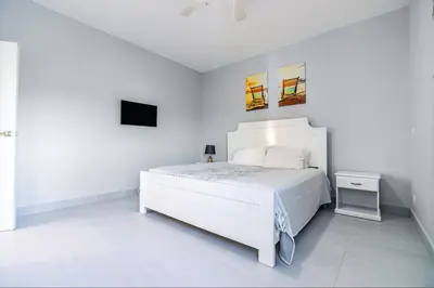 a white bedroom with a white bed and a tv at Villa real con piscina panorámica para más de 14 huéspedes in Sosúa