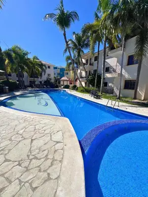 a blue swimming pool with palm trees and a building at Apartamento Rosa Hermosa in Punta Cana