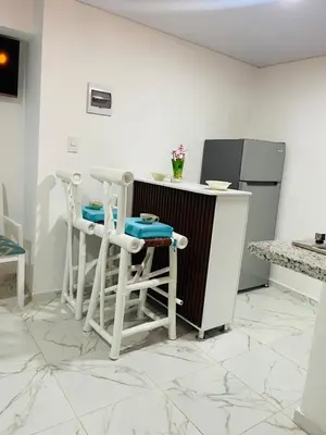 a kitchen with white stools and a counter with a refrigerator at Sabor Latino Apartment in San Felipe de Puerto Plata