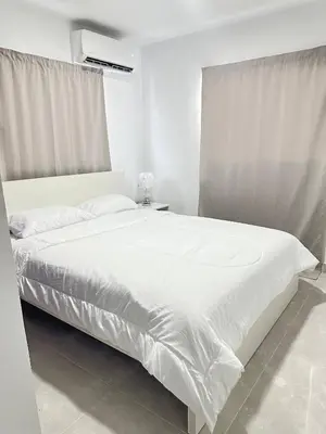 a white bedroom with a large bed with white sheets at Cozy Santo Domingo Apartment in San Isidro in Juan López