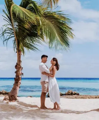 a bride and groom standing under a palm tree on the beach at Palmar Apartments Comfort Great Location in Punta Cana