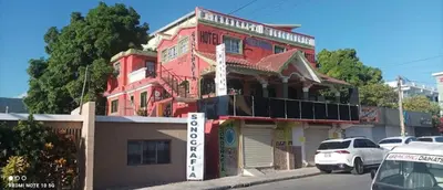 a red building on a street with cars parked in front at Hotel Pensión la Hermosa Barahona in Santa Cruz de Barahona