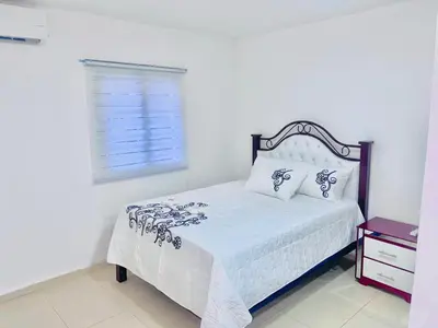 a white bedroom with a bed with white sheets and a window at Centrally located Comfortable Apartment in Bonao