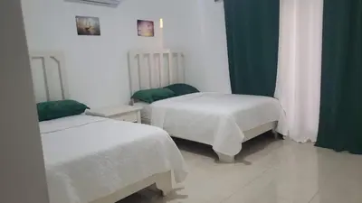 a bedroom with two beds with white sheets and green curtains at Hotel Dieux Internacional in Pedernales