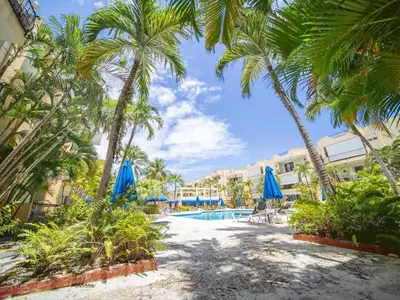 a resort pool with palm trees and blue umbrellas at Garden Condos 7 - Central Apartment in Strip in Sosúa