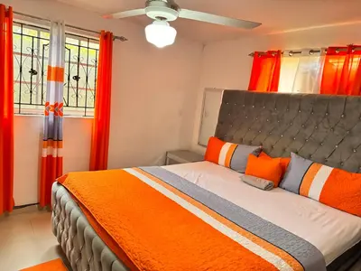 a bedroom with a bed with orange pillows and windows at Cozy Huge and Lovely 3 bedrooms apts 2bathdrooms in La Estrella