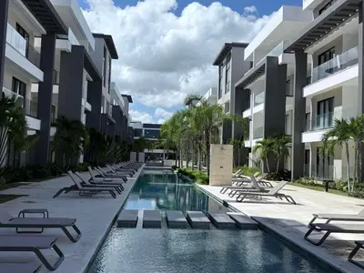 a swimming pool with chaise lounges and chairs next to buildings at Alexger Beachfront Apartament Bavaro, Punta Cana in Punta Cana