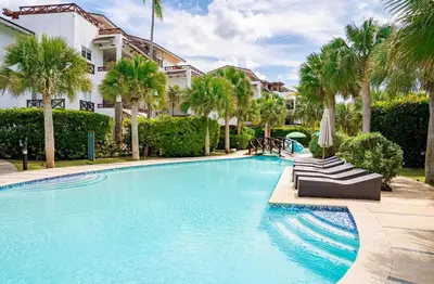 a swimming pool with palm trees and a building at Villa 1 min walk from the beach in Las Terranas in El Limón