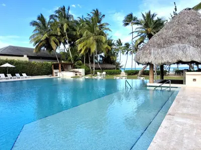 a swimming pool with a straw umbrella and palm trees at Gorgeous large condo, quiet beachfront complex in Las Terrenas