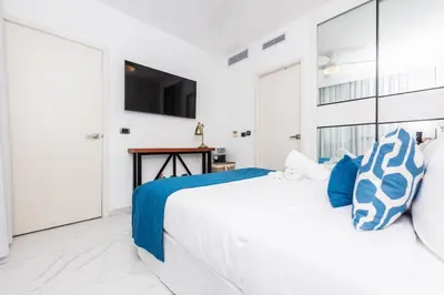 a white bedroom with a large bed with blue pillows at Luxury 2BR Private Jacuzzi CanaRock Star Punta Cana in Punta Cana