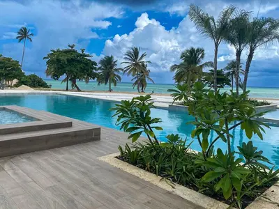 a swimming pool with palm trees and the ocean at Condominio de lujo Salida a playa Estilo Resort Muchas comodidades: 6 piscinas/TV/aire acondicionado in Punta Cana