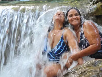 two people sitting on rocks in front of a waterfall at 2 Bdrm, Wi-fi, Hot Water Near Beach and River, 2R in Paraíso