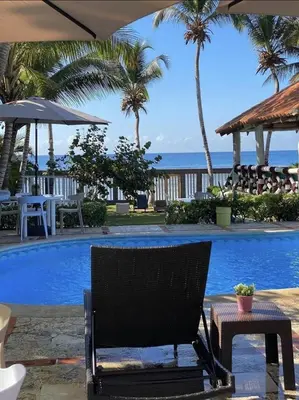 a chair next to a swimming pool with palm trees at Arena blanca Franchecis hostal in Juan Dolio