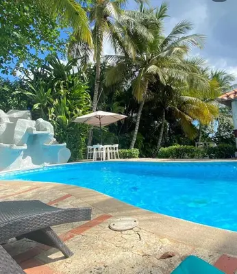 a swimming pool with a table and an umbrella at El Mar Azul Franchecis hostal in Juan Dolio