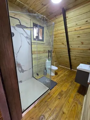 a bathroom with a glass shower in a wooden cabin at Cabaña Silencio Verde in Jarabacoa