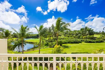 a view from the balcony of a resort with palm trees and a pond at Iberostate 2BR Apartment - BBQ, Terrace, Lake & Golf Views, Beach Club Access in Punta Cana