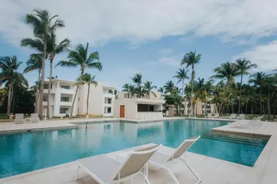 a swimming pool with white chairs and palm trees at Caribe Deluxe Princess - All Inclusive in Punta Cana