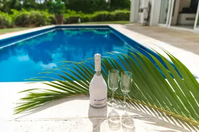 a bottle and two wine glasses sitting next to a swimming pool at Luxury Private Villas with Pool, Private Beach, BBQ in Punta Cana