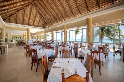 a restaurant with white tables and chairs and windows at Viva Dominicus Beach by Wyndham, A Trademark All Inclusive in Bayahibe