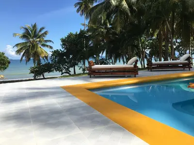 a swimming pool with two benches next to the ocean at Casa Altea in Santa Bárbara de Samaná