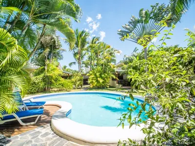 a swimming pool in front of a villa with palm trees at Résidence Villas Les Hibiscus in Las Terrenas