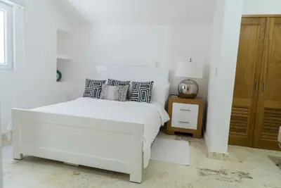 a white bedroom with a bed and a night stand at 3BR / 3BA Modern Paradise Loft Condo in Gated Community w/ Daily Housekeeping in Sosúa