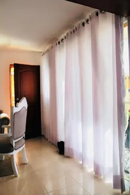 a living room with white curtains and a chair at Apartamento Los Rieles in Santiago de los Caballeros