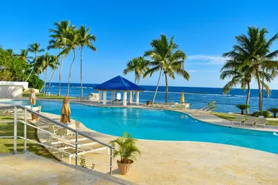 a resort swimming pool with the ocean in the background at Las Olas by Destinos1a in Juan Dolio