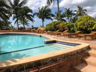 a swimming pool with benches and palm trees in a resort at La Cueva del Che in Juan Dolio