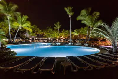 a pool with chairs and palm trees at night at Playabachata in San Felipe de Puerto Plata