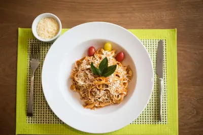 a white bowl of spaghetti with tomatoes and a green garnishment at Hampton By Hilton Santo Domingo Airport in Boca Chica
