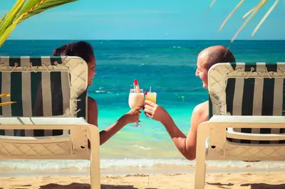 a man and woman sitting on the beach with drinks at Hotel Playa Colibri in Las Terrenas