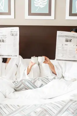 a person laying in bed reading a newspaper and drinking coffee at Hodelpa Centro Plaza in Santiago de los Caballeros