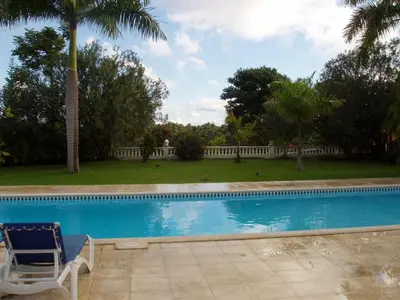 a blue swimming pool with a chair and a palm tree at 3br Villa with Vip Access - All Inclusive Program with Alcohol Included in San Felipe de Puerto Plata