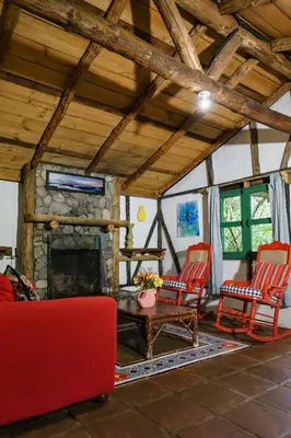 a living room with a stone fireplace and red chairs at Villa Pajon Eco Lodge in Constanza
