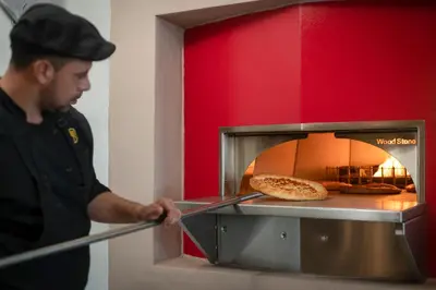 a man is putting a pizza in an oven at Presidential Suites Cabarete - Room Only in Cabarete