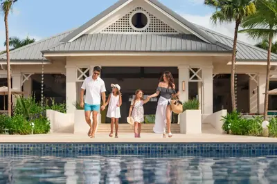 a family standing by a swimming pool in front of a house at Dreams La Romana All-Inclusive Resort & Spa in Bayahibe